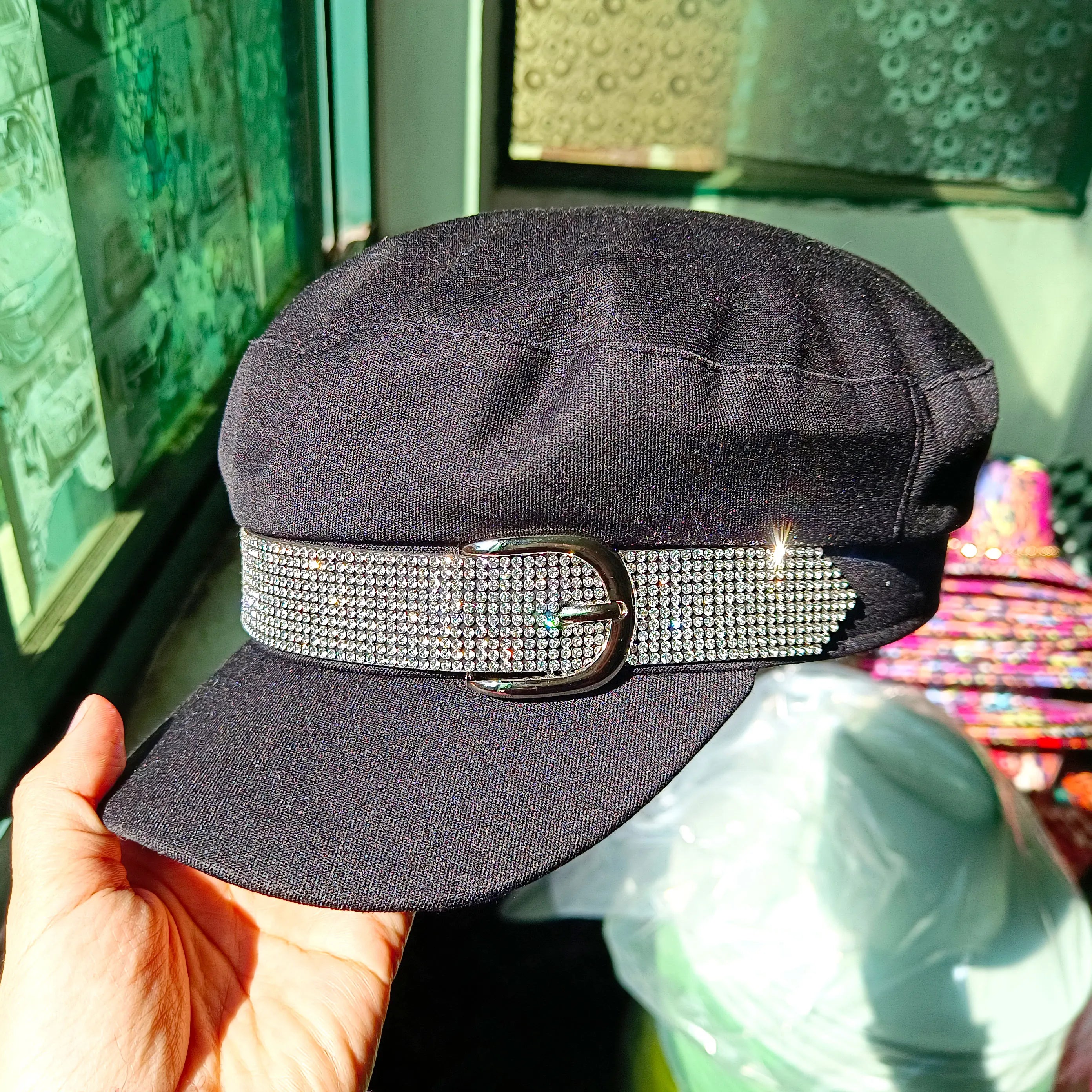 Black peaked cap with a rhinestone-embellished decorative belt and buckle feature.