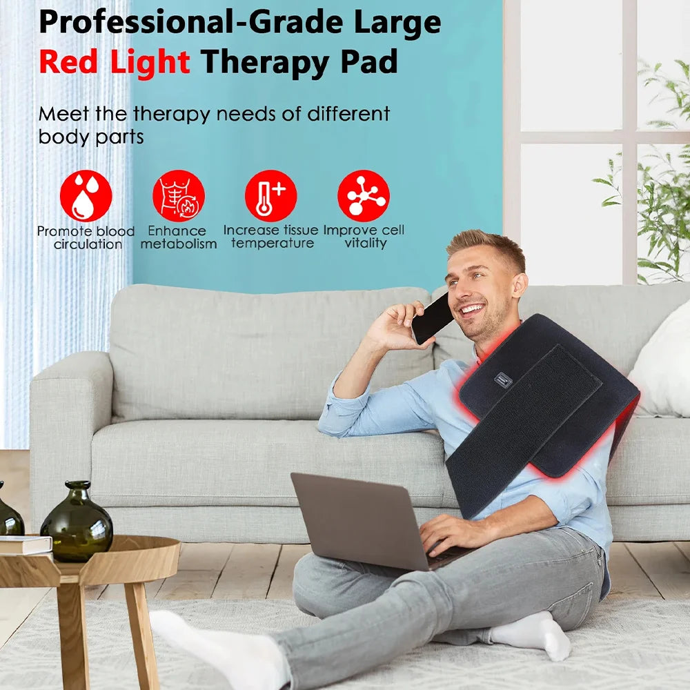 Man on phone with red light therapy pad draped over his shoulder while working on a laptop.