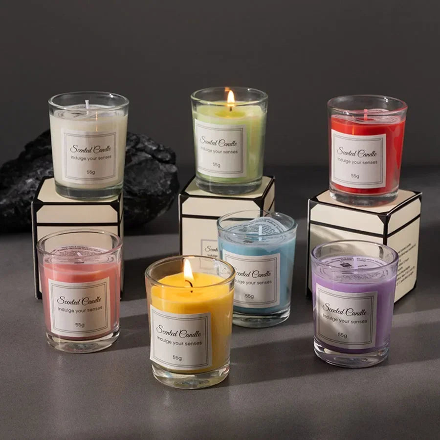 Six colourful 55g scented candles in glass jars, with some lit, displayed on small boxes against a grey background.