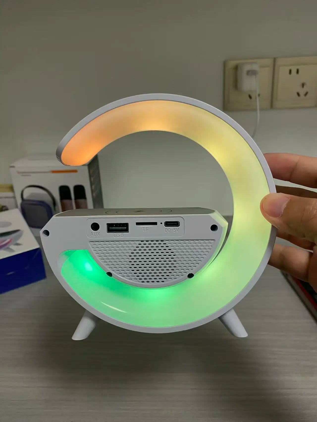 White crescent-shaped alarm clock with a colour-changing LED light, wireless charging base, and built-in ports.