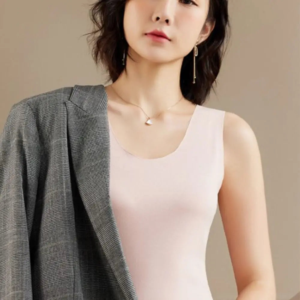 A woman wearing a pale pink sleeveless vest top layered with a grey plaid blazer.