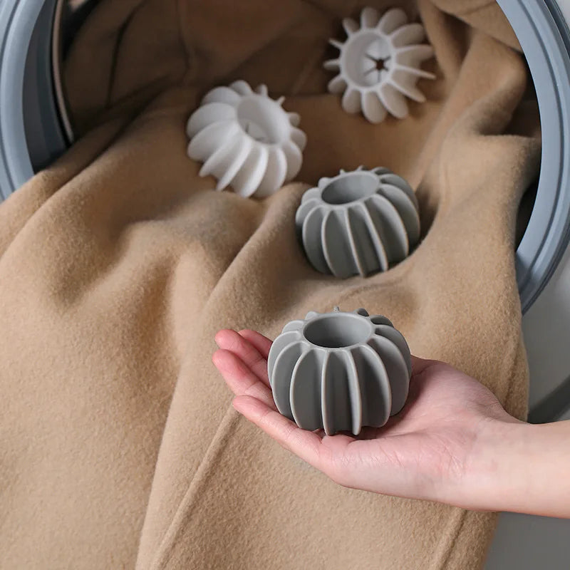 Hand holding a ribbed grey laundry dryer ball, with white and grey dryer balls on a blanket inside a tumble dryer.