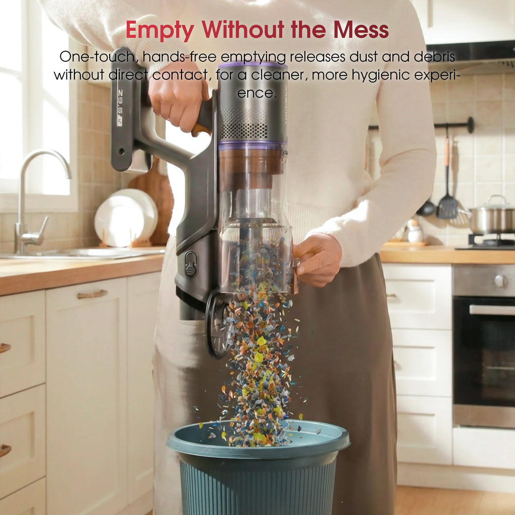 Grey cordless stick vacuum emptying dustbin contents into a trash can in a kitchen.