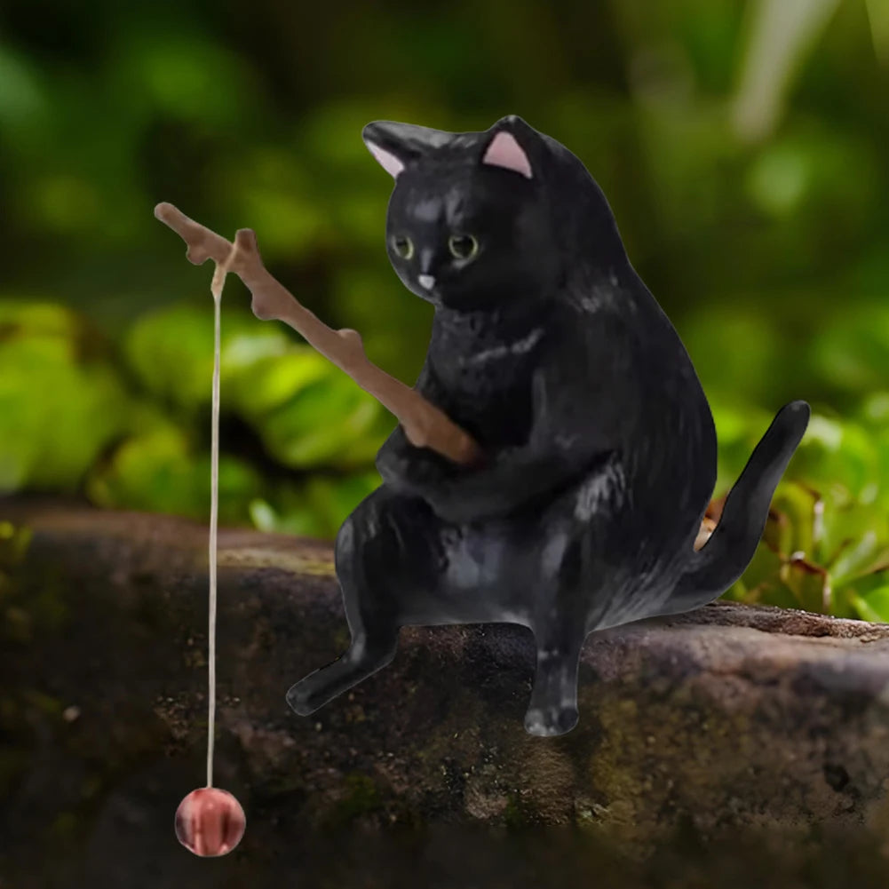 A cute, black cat aquarium ornament holding a wooden fishing rod with a dangling line and bait.