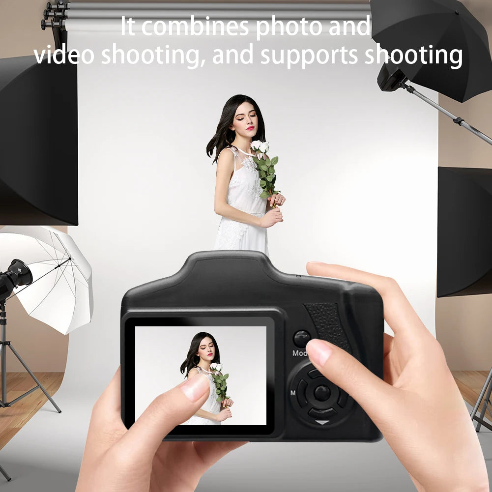 Black plastic digital camera with a rear LCD screen, held in hands, displaying a live image of a woman.