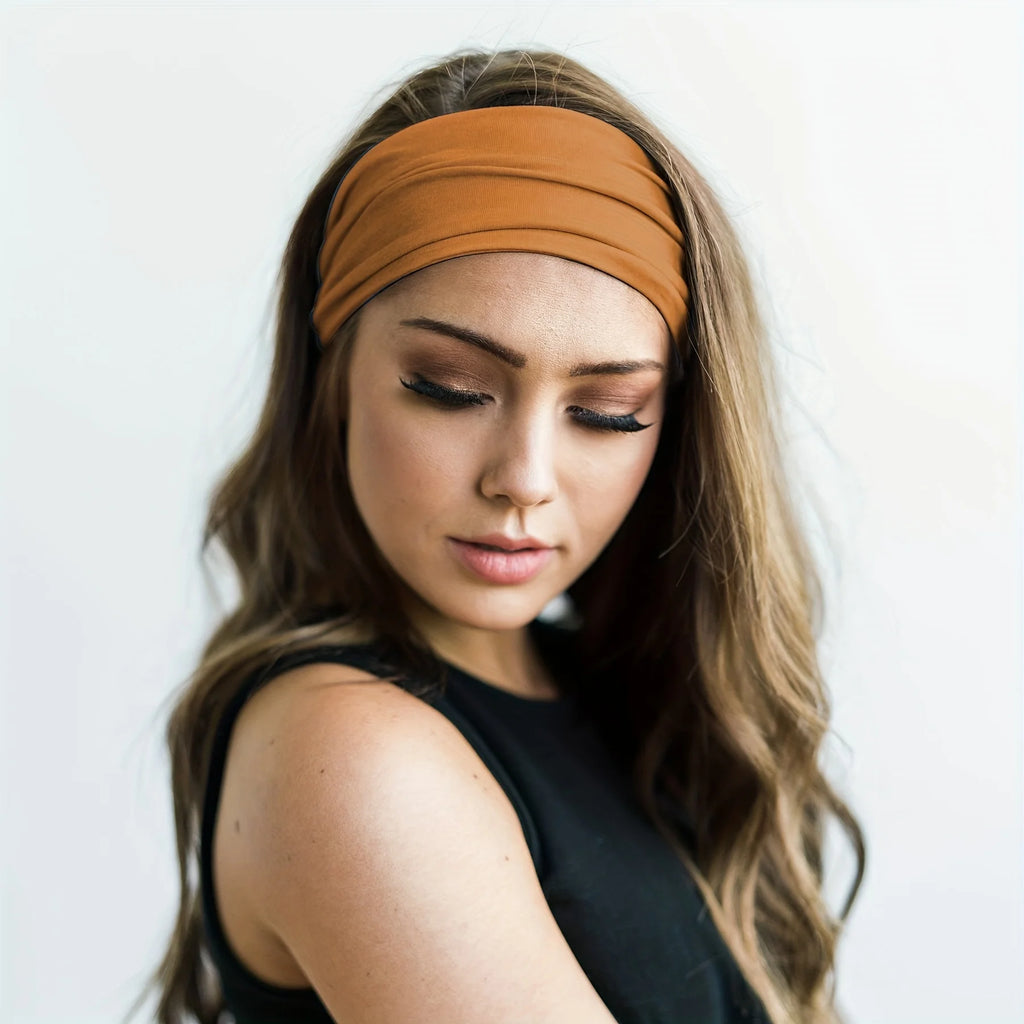 Model wearing a plain, wide, ochre-brown fabric headband with a soft, gathered finish.