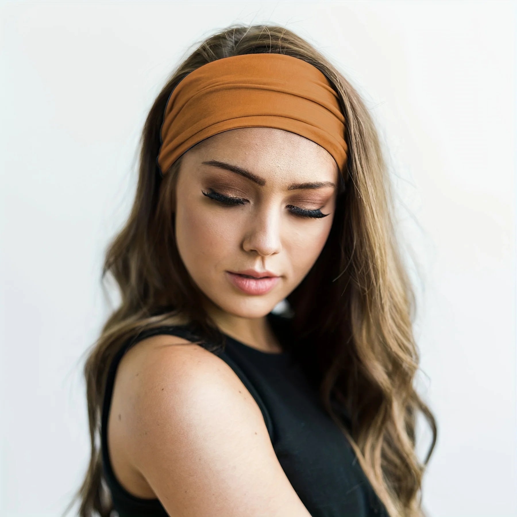 Model wearing a plain, wide, ochre-brown fabric headband with a soft, gathered finish.