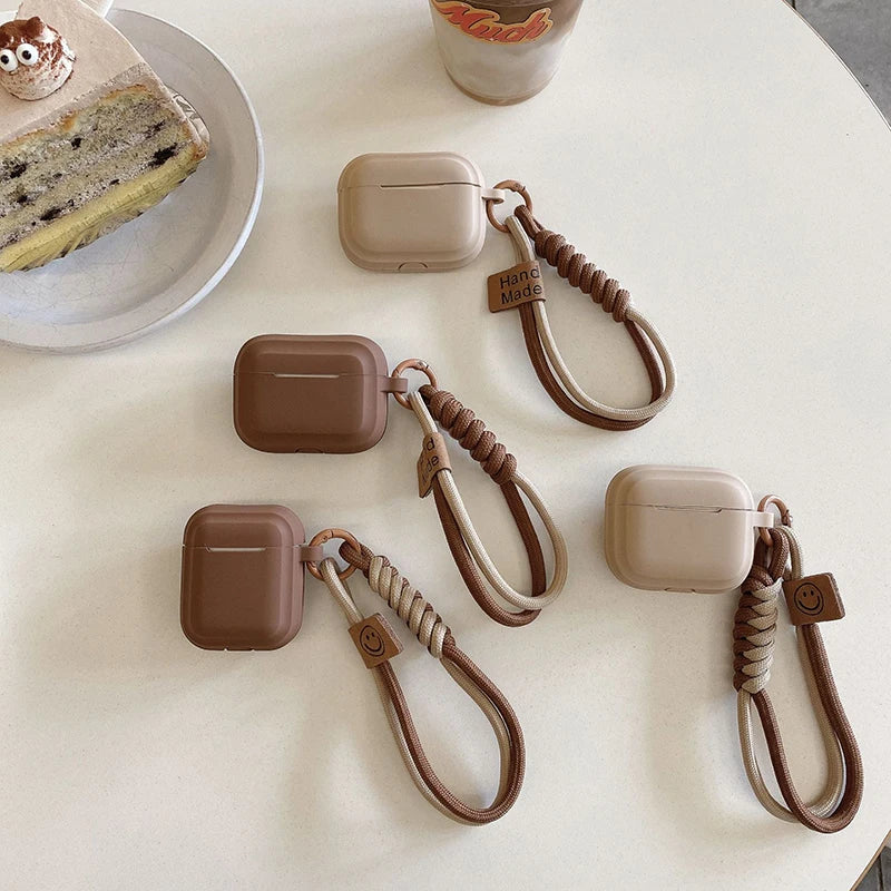 Beige and brown silicone AirPods cases with braided wrist straps and 'Handmade' or smiley face tags.
