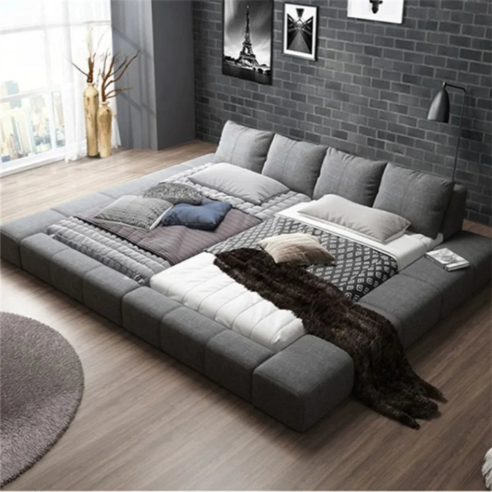 Modern, grey upholstered double bed with a wide padded headboard and low-profile frame in a contemporary bedroom.