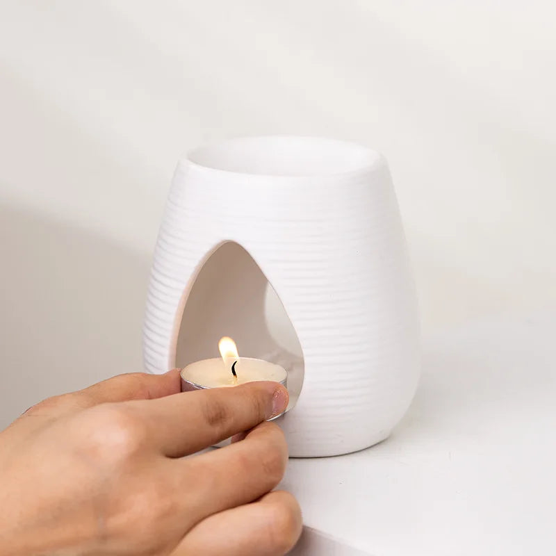 Hand placing a lit tealight into a white, ribbed ceramic wax melt burner with an arched cutout.