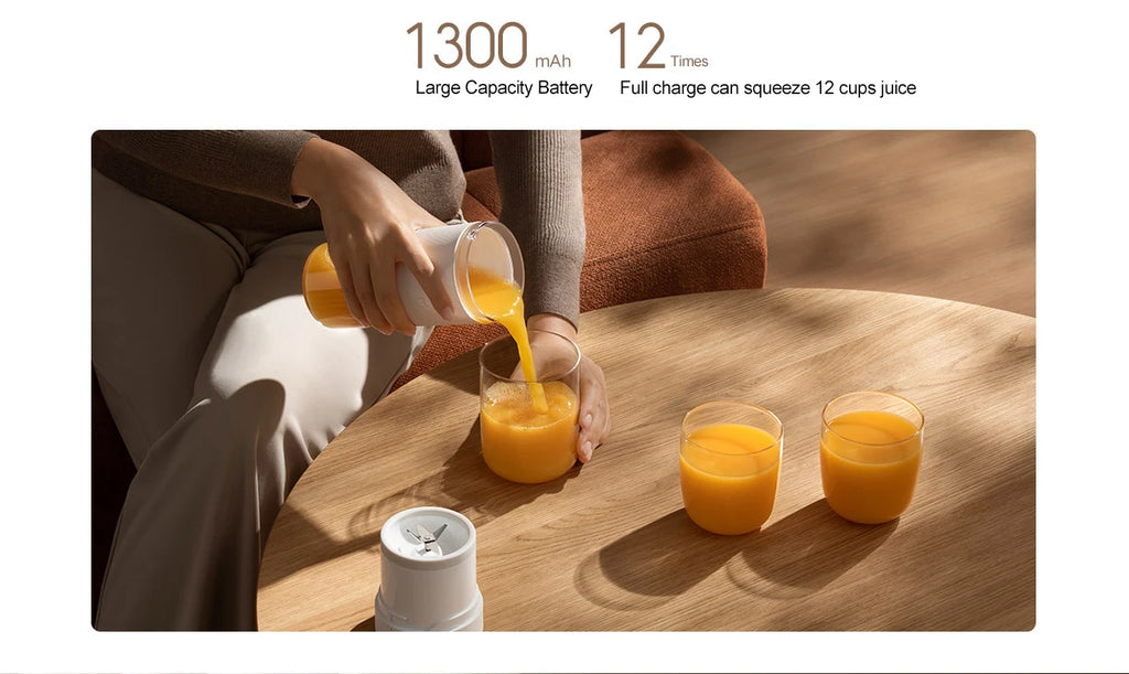 A person pouring orange juice from a sleek, white portable blender cup into glasses on a wooden table.