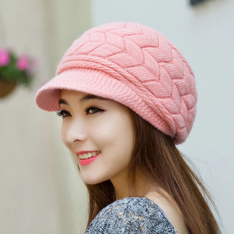 A woman wears a soft pink, cable-knit thermal baker boy hat with a textured pattern and a short peak.