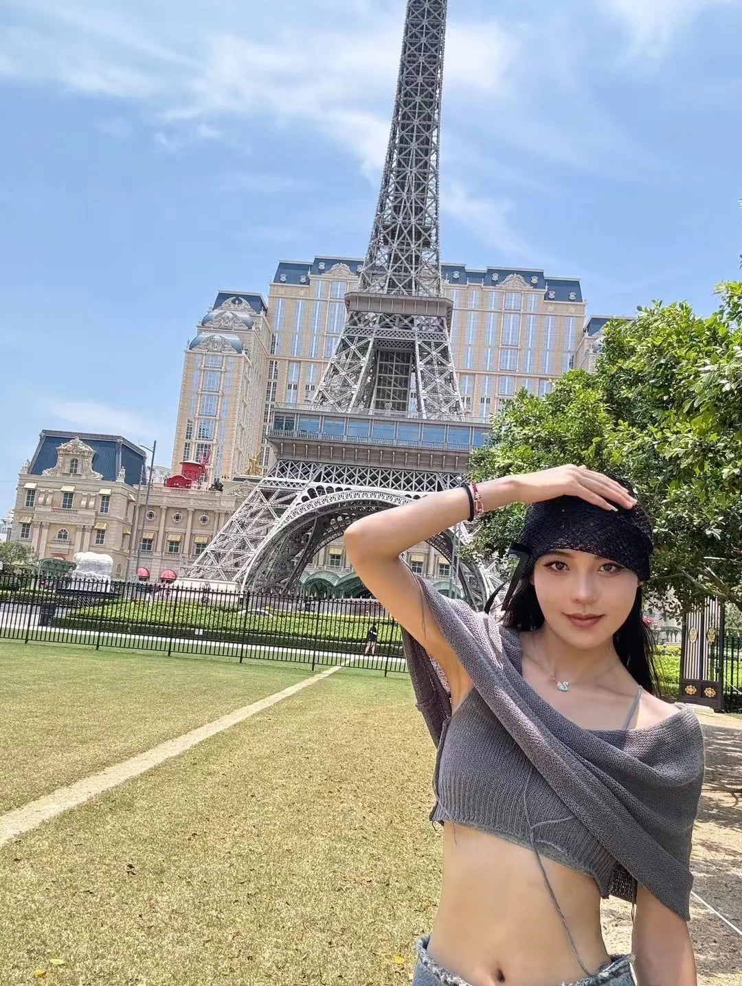 A woman wearing a black, elegant, open-knit beanie with a side bow detail, with the Eiffel Tower in the background.