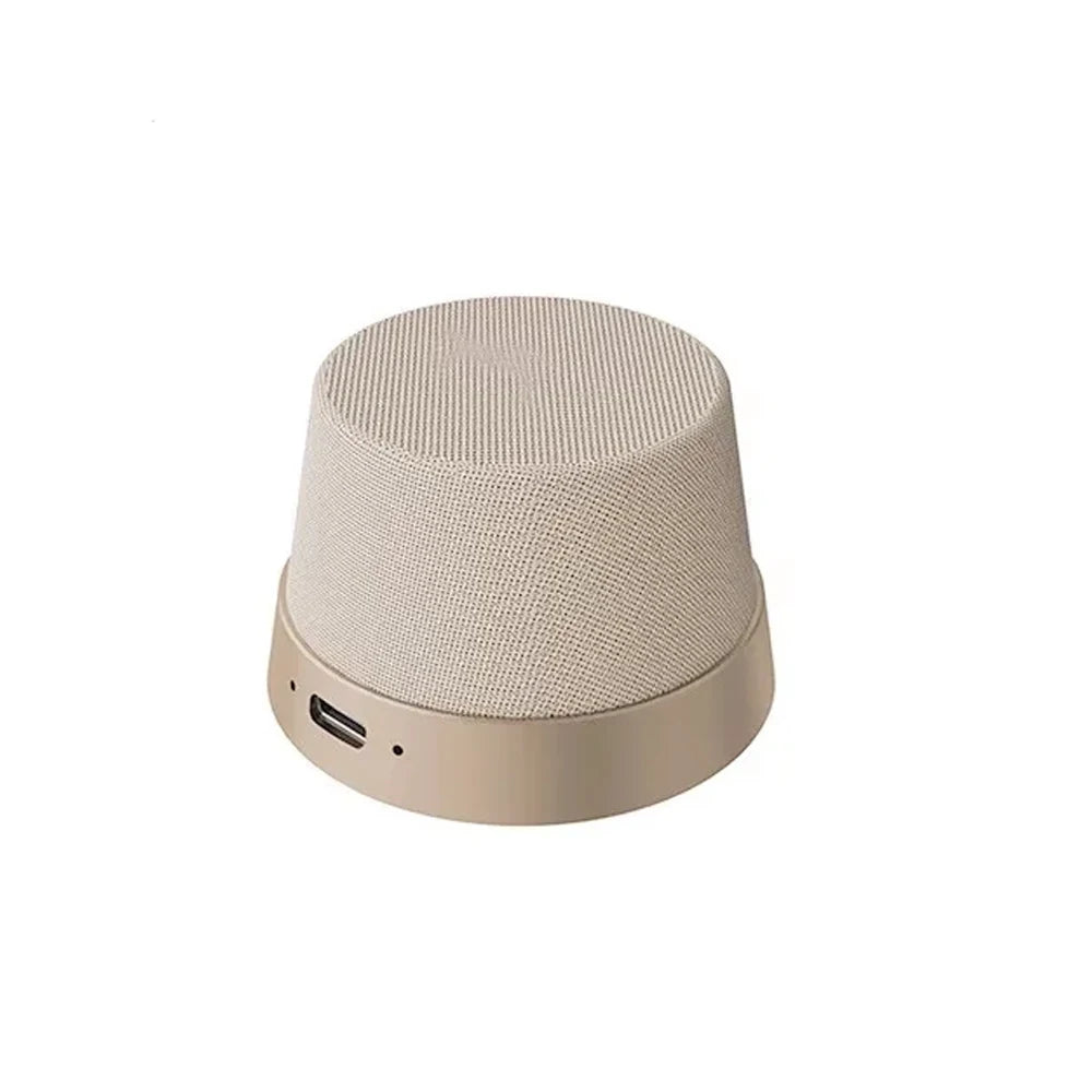 Compact, beige fabric-covered magnetic wireless speaker with a smooth metallic base and a charging port.