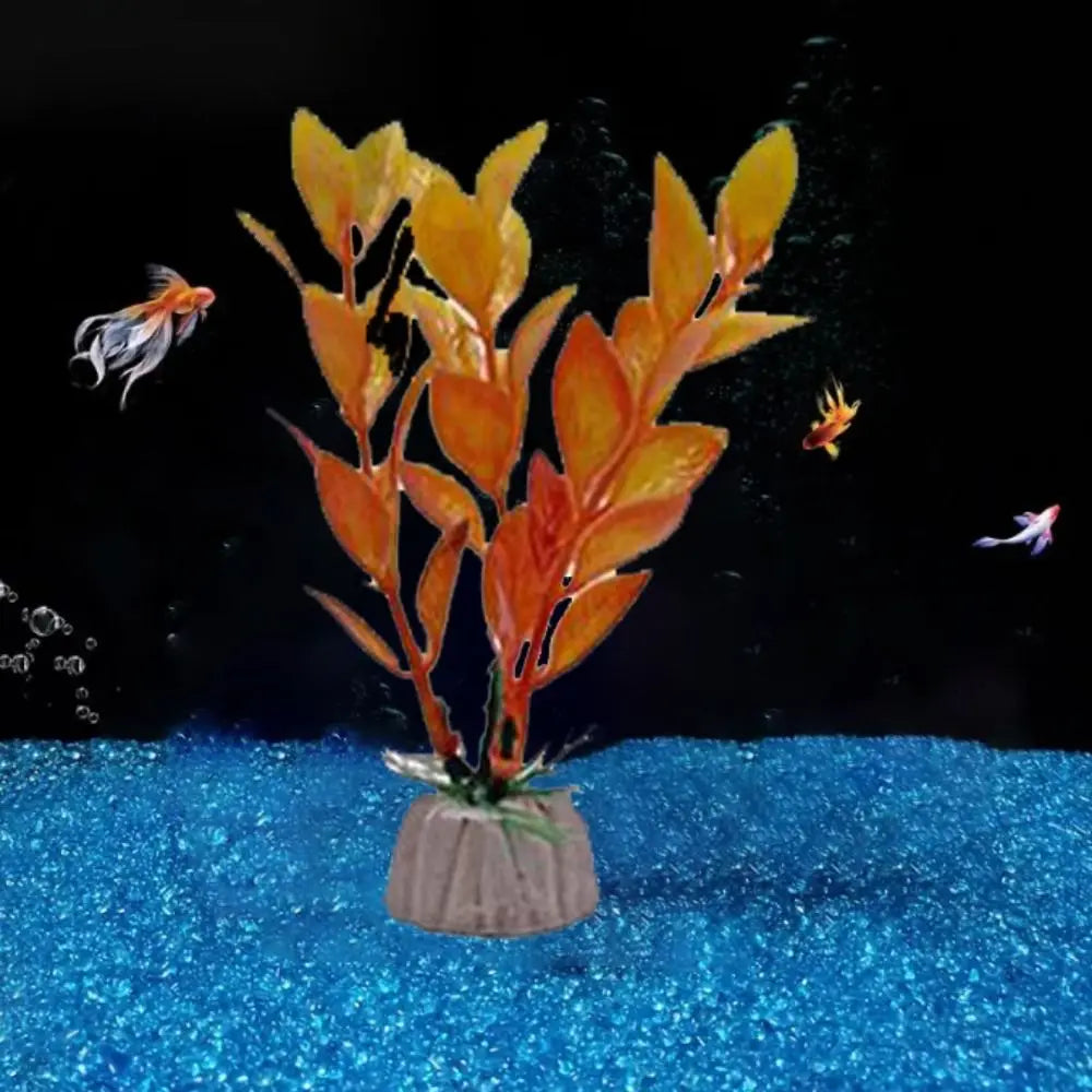 Artificial orange plastic aquarium plant on a tan base, set against a black background with blue gravel and small fish.