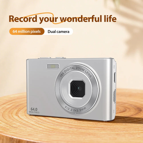 Silver compact digital camera with 64MP dual lens and 18x digital zoom on a wooden surface.