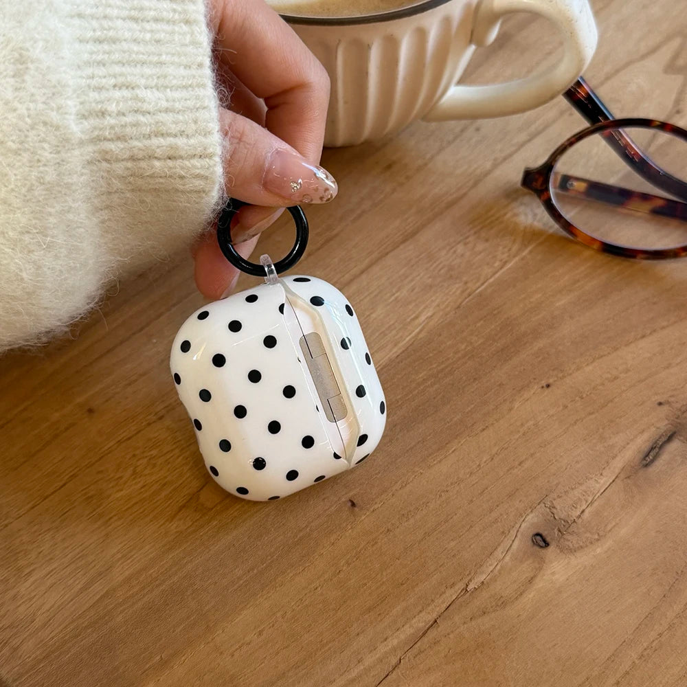 White hard-shell AirPods case with black polka dots and a circular carabiner ring.