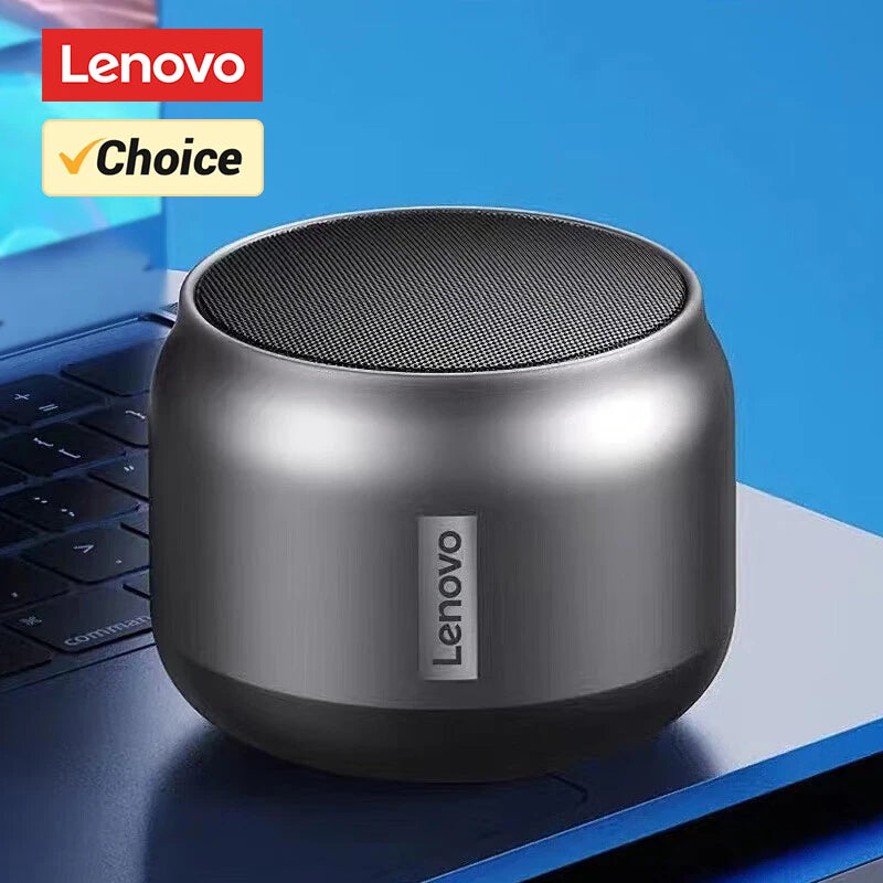 Compact, metallic grey wireless speaker with a circular top-mounted mesh grille, resting on a laptop.