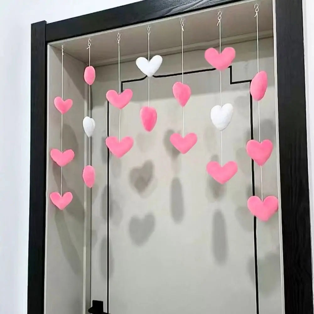Pink and white heart-shaped ornaments hanging from strings in a doorway, creating a decorative mobile effect.