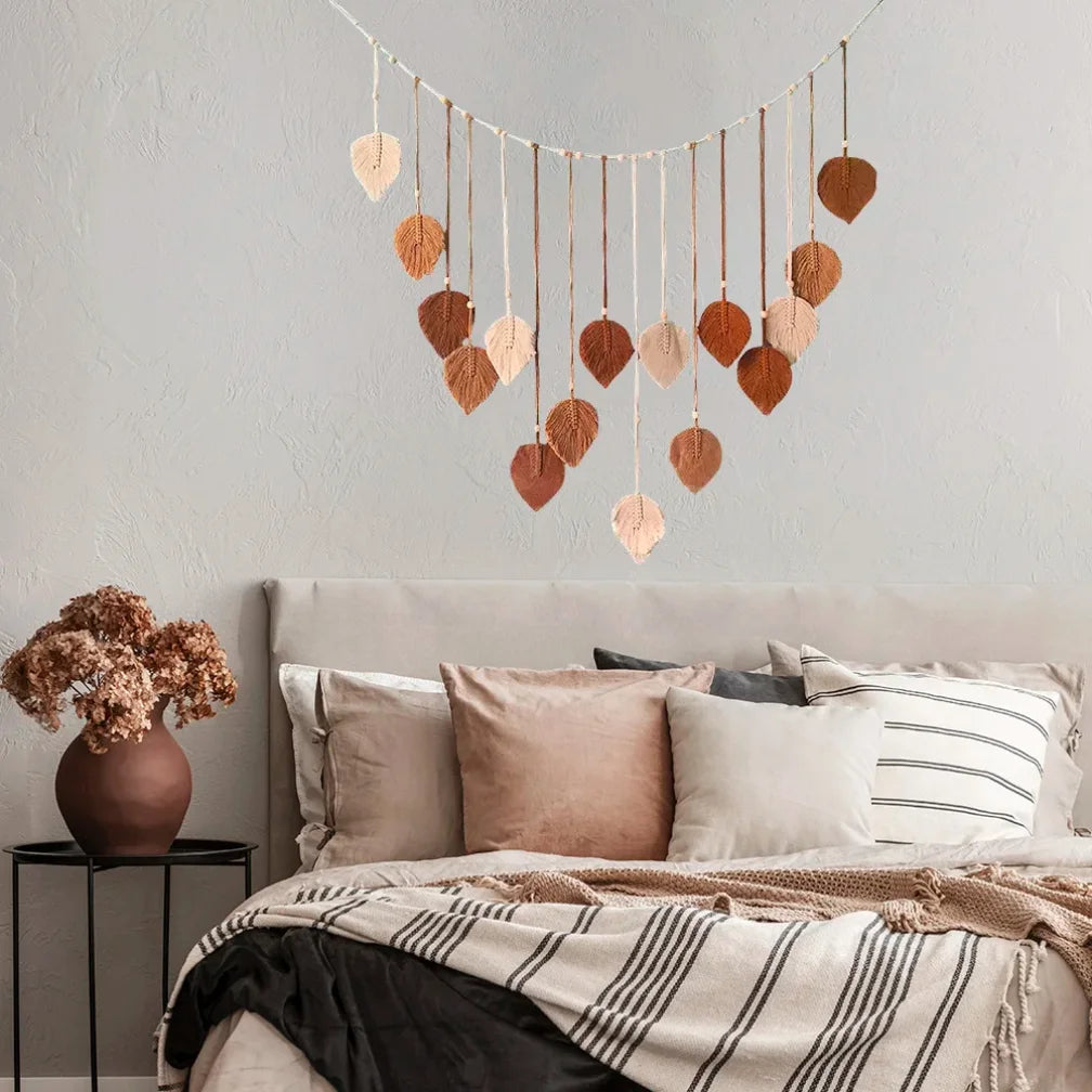 Boho macrame wall hanging featuring dangling cream and brown leaf-shaped tassels, displayed above a neutral bedroom bed.