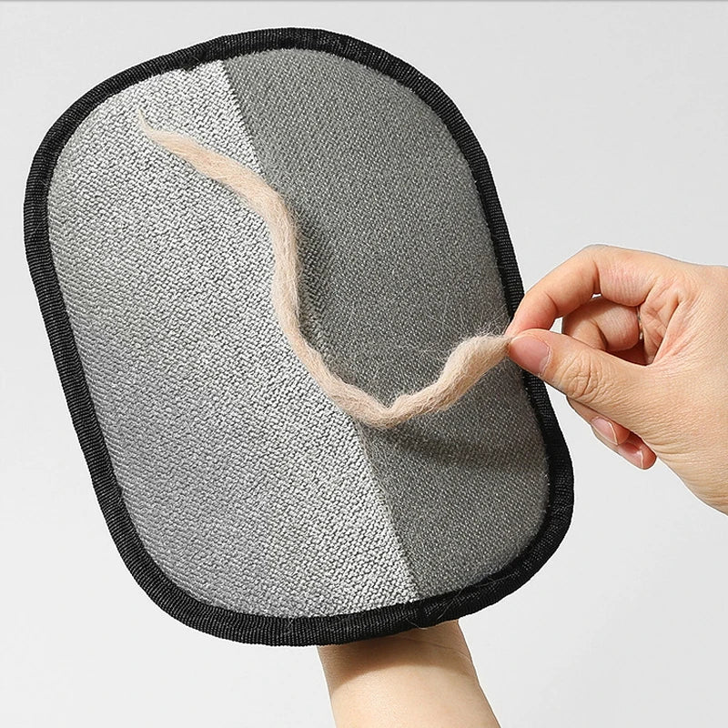 A person holding a grey and white lint-removing mitt, shown lifting a strand of beige pet hair off the surface.