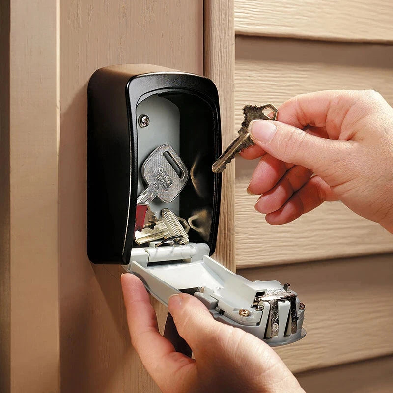 Black metal wall-mounted key lock box with a hinged door, being opened by hands to store or retrieve keys.