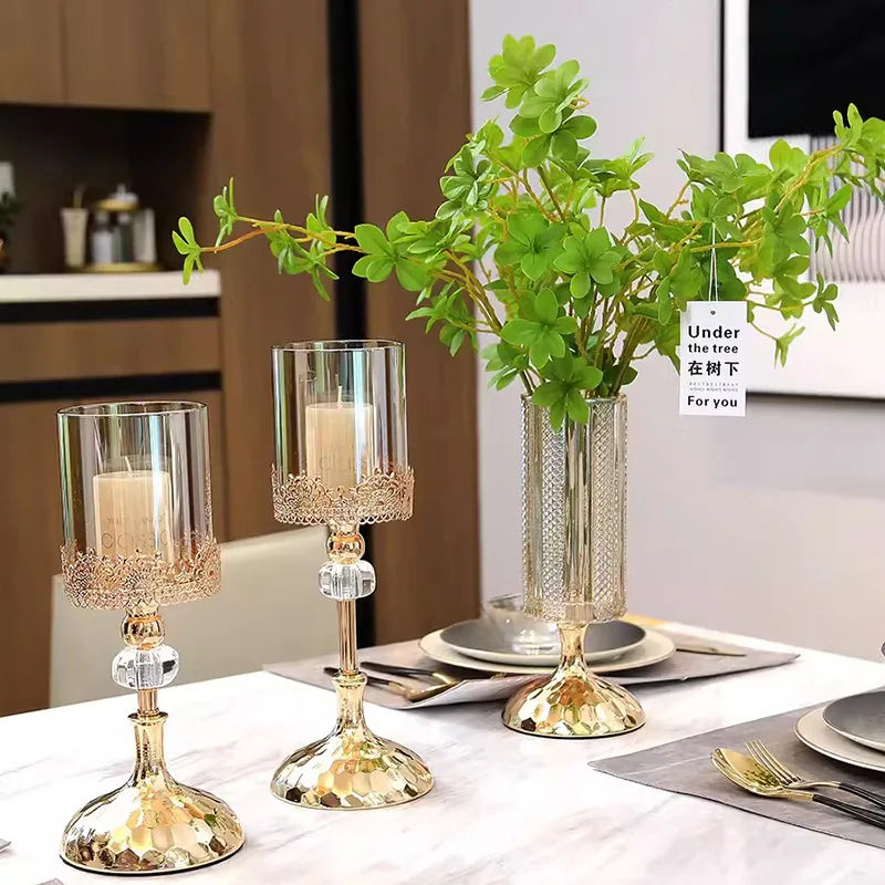 Gold crystal candle holders with glass cylinders and white pillar candles on a dining table.