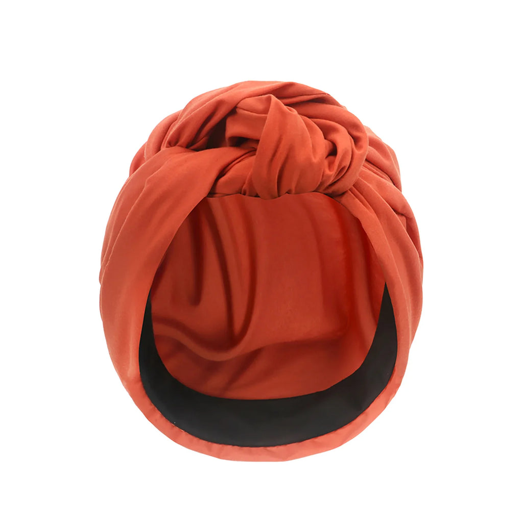 A vintage-style burnt orange turban hat featuring a front knot detail and a smooth, wide black inner brim.