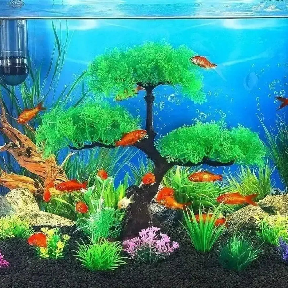Artificial green bonsai tree in an aquarium with goldfish, black gravel, and small pink plants.
