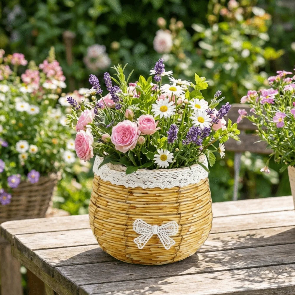 A rustic woven basket filled with pink roses, daisies, and lavender, decorated with white lace trim and a small bow.