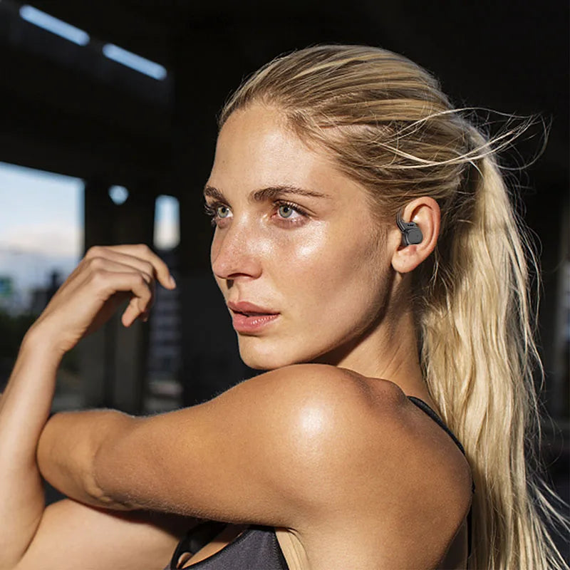 A woman wearing sleek, grey, compact wireless ear hooks while stretching in a fitness setting.