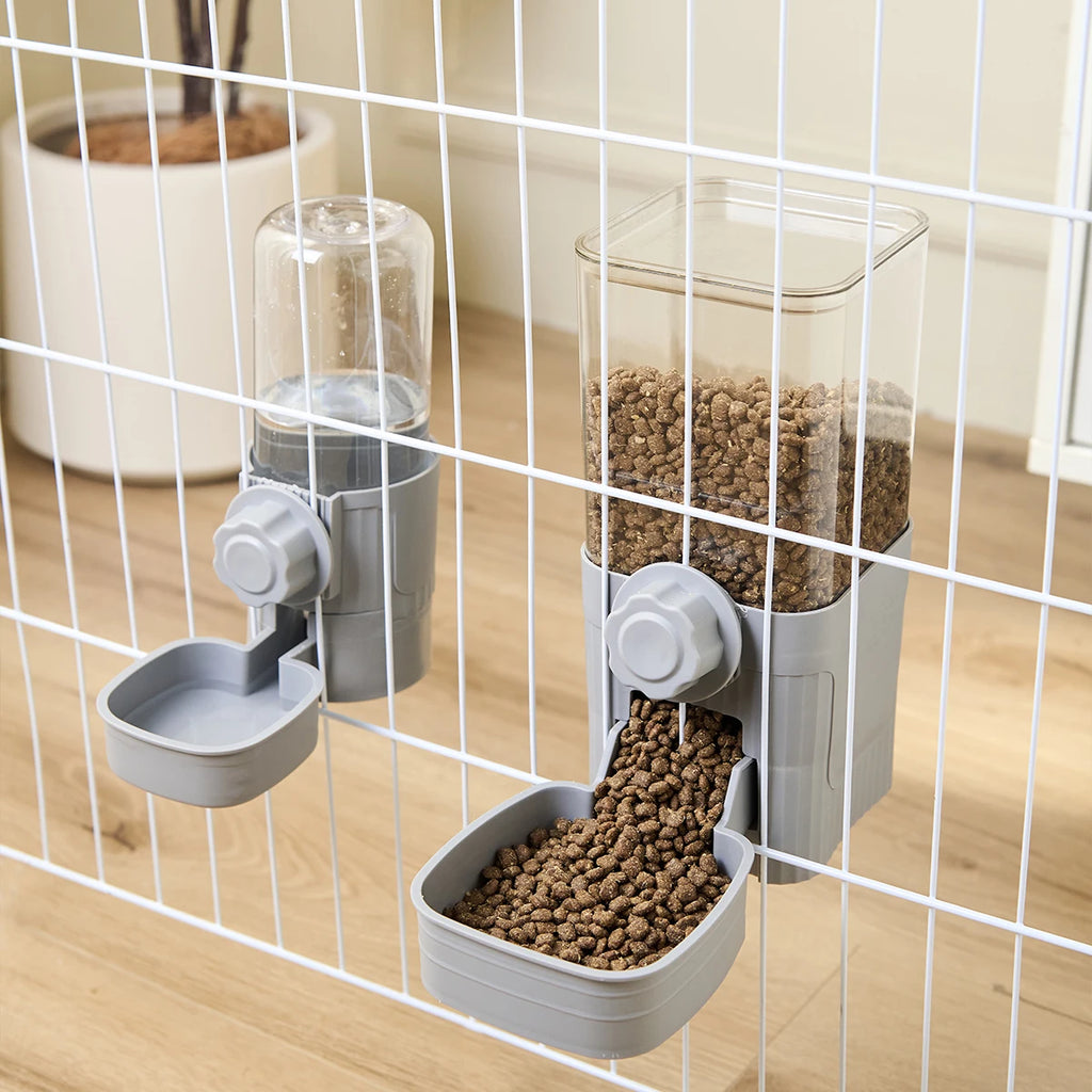 Gray hanging pet water and food dispensers attached to a white wire cage, featuring clear containers.