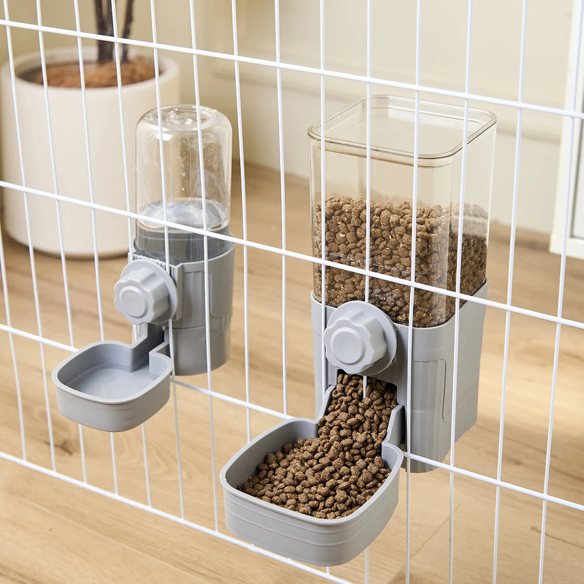 Gray hanging pet water and food dispensers attached to a white wire cage, featuring clear containers.