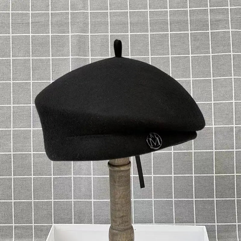 Classic black wool felt beret with a small top bobble and a decorative silver circular badge on the side.