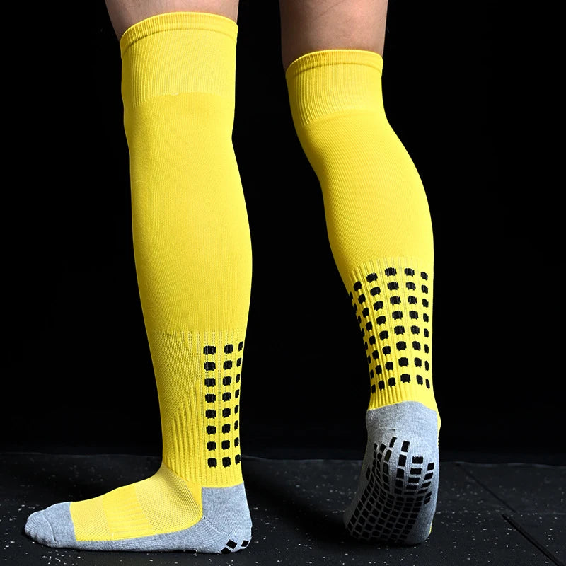 Yellow over-the-knee sports socks with black grip pads and grey heel and toe sections against a black background.
