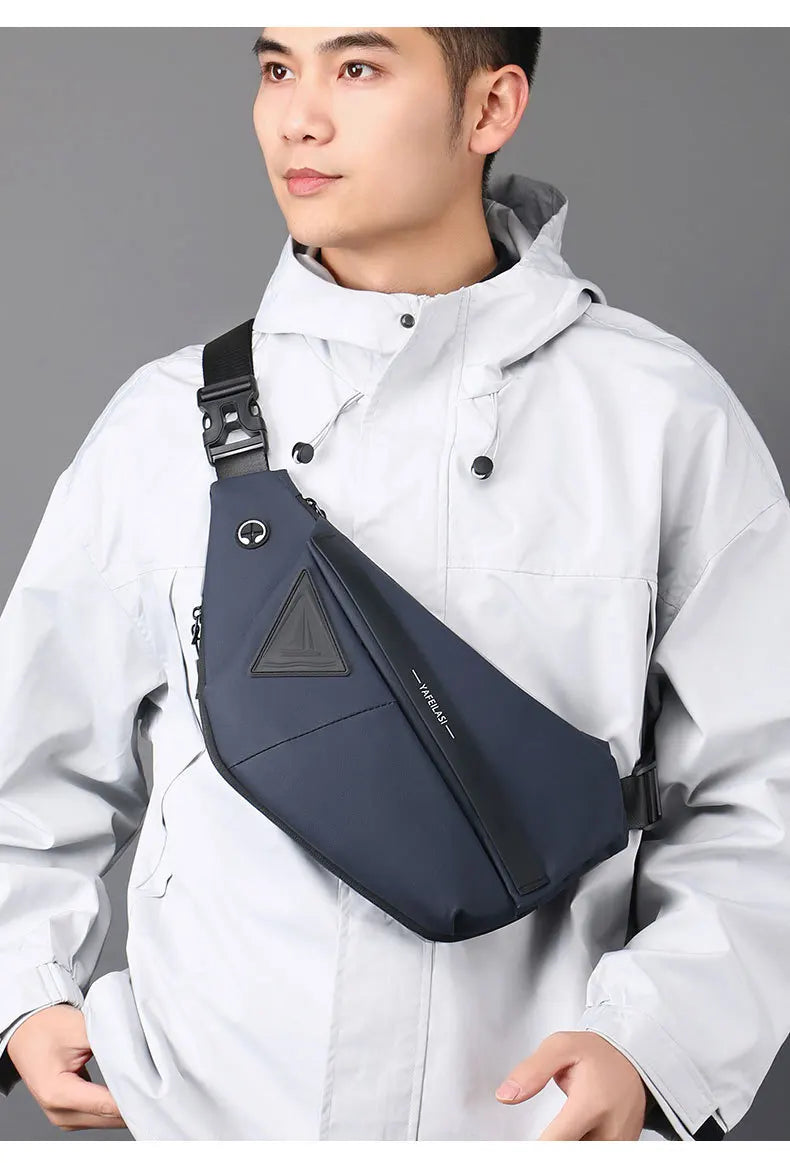 A man wearing a slim, dark blue anti-theft crossbody sling bag with a secure buckle strap and headphone port.