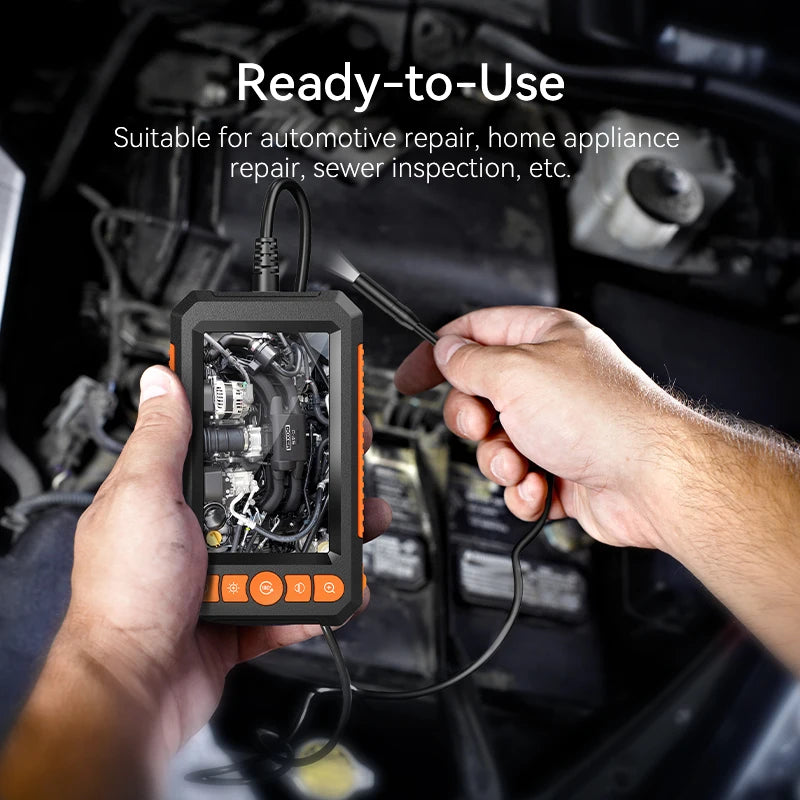 Handheld black and orange industrial borescope with a clear screen, being used to inspect a vehicle engine bay.