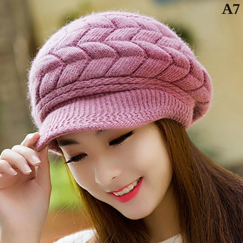 A woman wearing a cosy, dusky pink cable-knit peaked cap with a soft faux-fur lining.