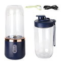 Portable blender in navy with rose gold trim, extra bottle, green peeler, and USB charging cable on white background.
