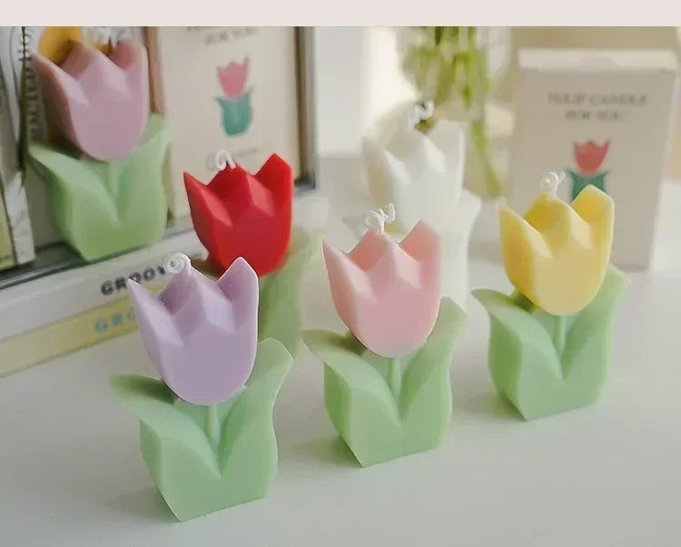 A collection of geometric, tulip-shaped candles in various colours, each with green leaves and a small candle wick.