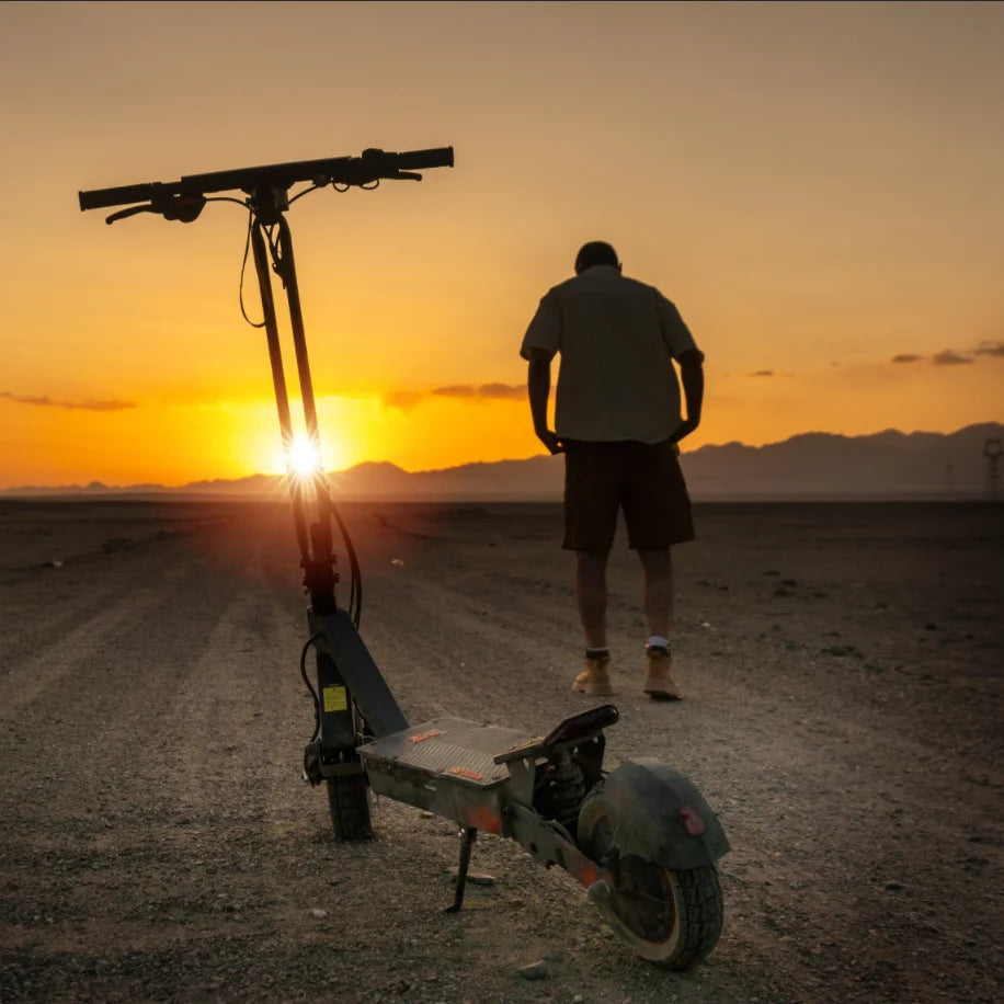 Black dual-motor electric scooter with 10-inch tires and wide deck parked outdoors at sunset.