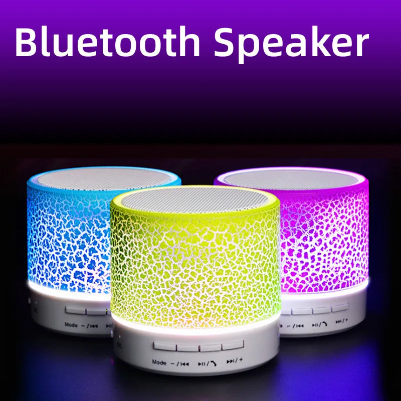 Three portable mini Bluetooth speakers with glowing, cracked-pattern LED shells in blue, neon yellow, and purple.