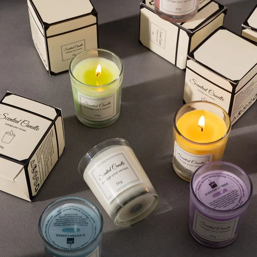 A collection of colourful scented candles in glass jars, each with a matching gift box on a grey surface.