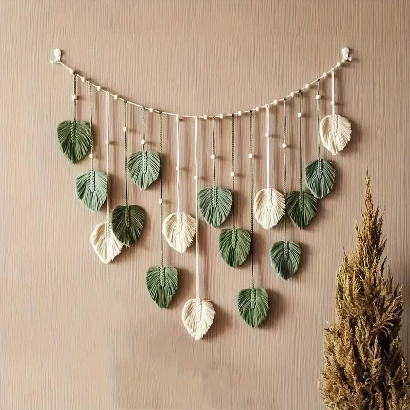 Boho macrame wall hanging featuring sage green and cream leaf motifs on a beaded string.