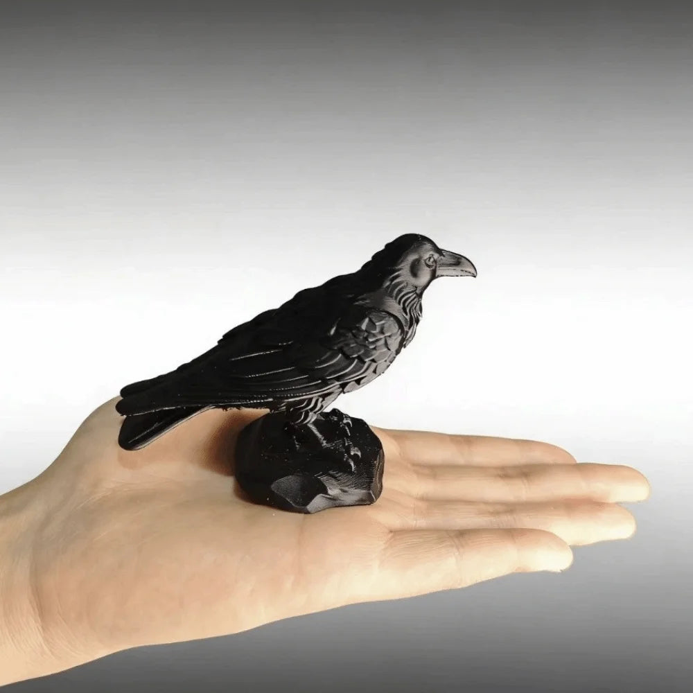 Small black raven figurine with realistic feather detailing, resting on a stone base and held in an open hand.