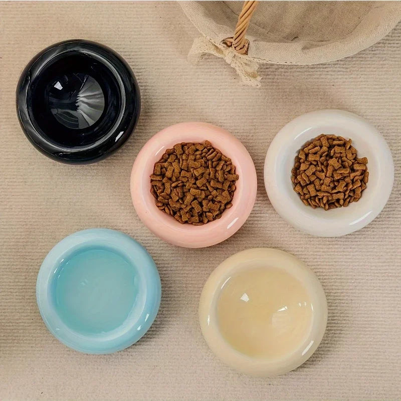 Top-down view of five round, glossy ceramic cat feeding bowls in black, pink, white, blue, and cream.