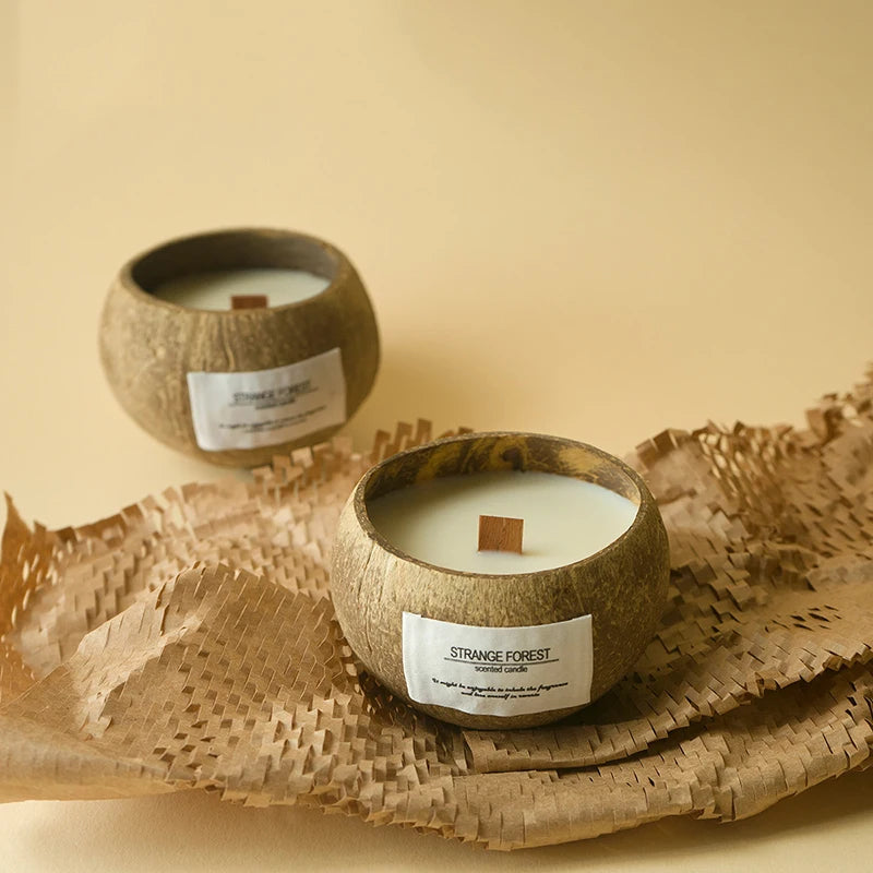 Two scented candles in natural coconut shell holders with wooden wicks, set on textured brown paper packaging.
