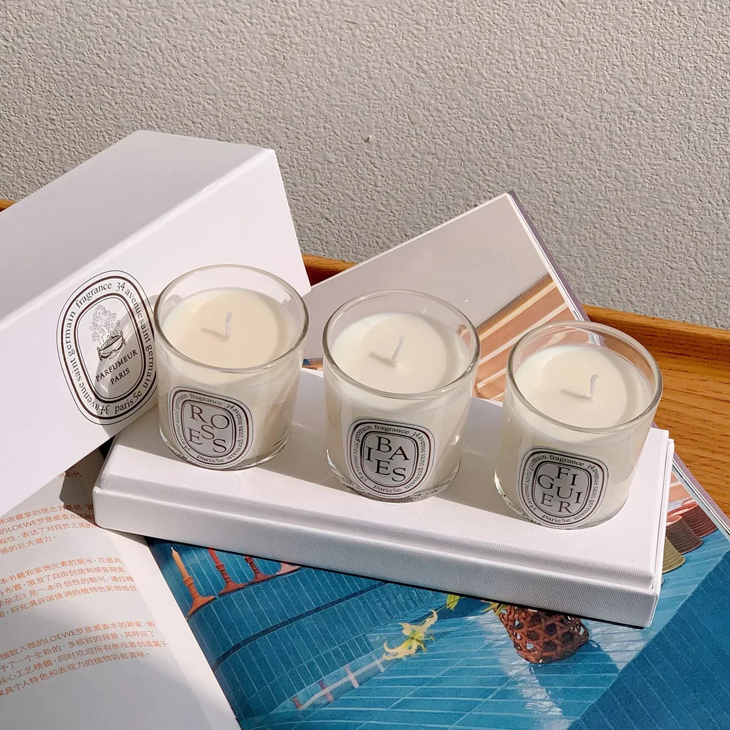 A luxury gift set of three white scented candles in clear glass jars with elegant circular labels on a white tray.