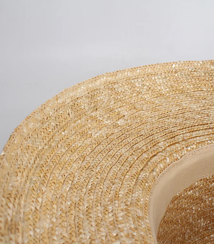Close-up of a natural beige straw sun hat with a wide brim and smooth inner ribbon detail.