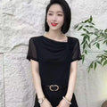Woman wearing a black short-sleeved top with a draped neckline, sheer mesh sleeves, and a small floral embellishment.